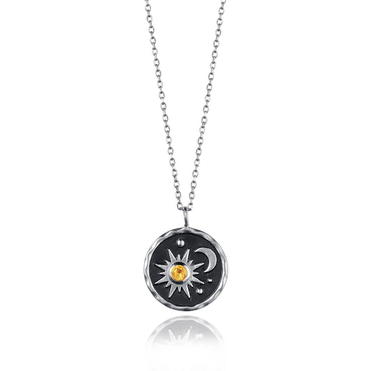 Round coin shaped necklace with black centre and a sun and moon motif set with an orange citrine stone