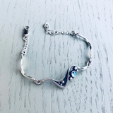 Silver bracelet featuring ripple and bubble design with round blue topaz stone and three links