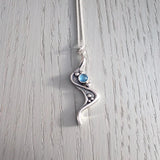 A silver pendant with ripple and bubble design and a round blue topaz stone