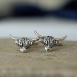 A pair of silver cufflinks shaped like Highland cow heads with simple T-bar clasps and oxidised details on table