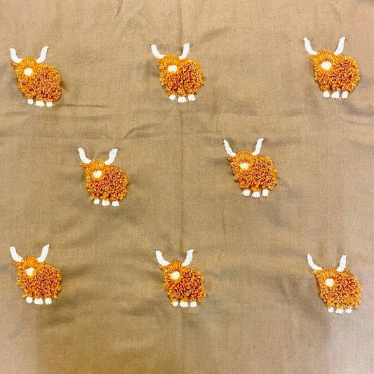 A beige coloured scarf with embroidered fluffy Highland cows pattern