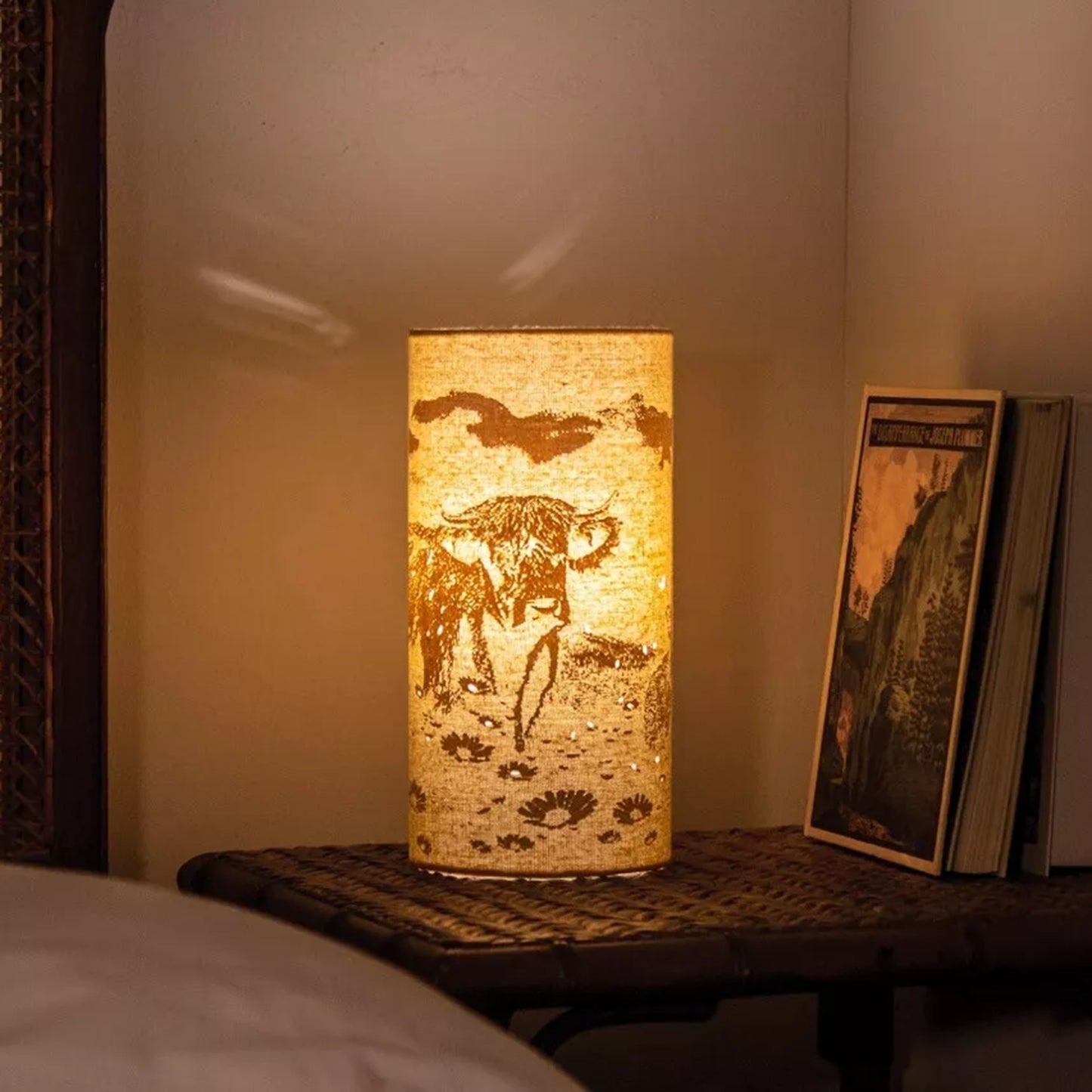 A linen look fabric table lamp with a Highland cow design and cut out details lifestyle