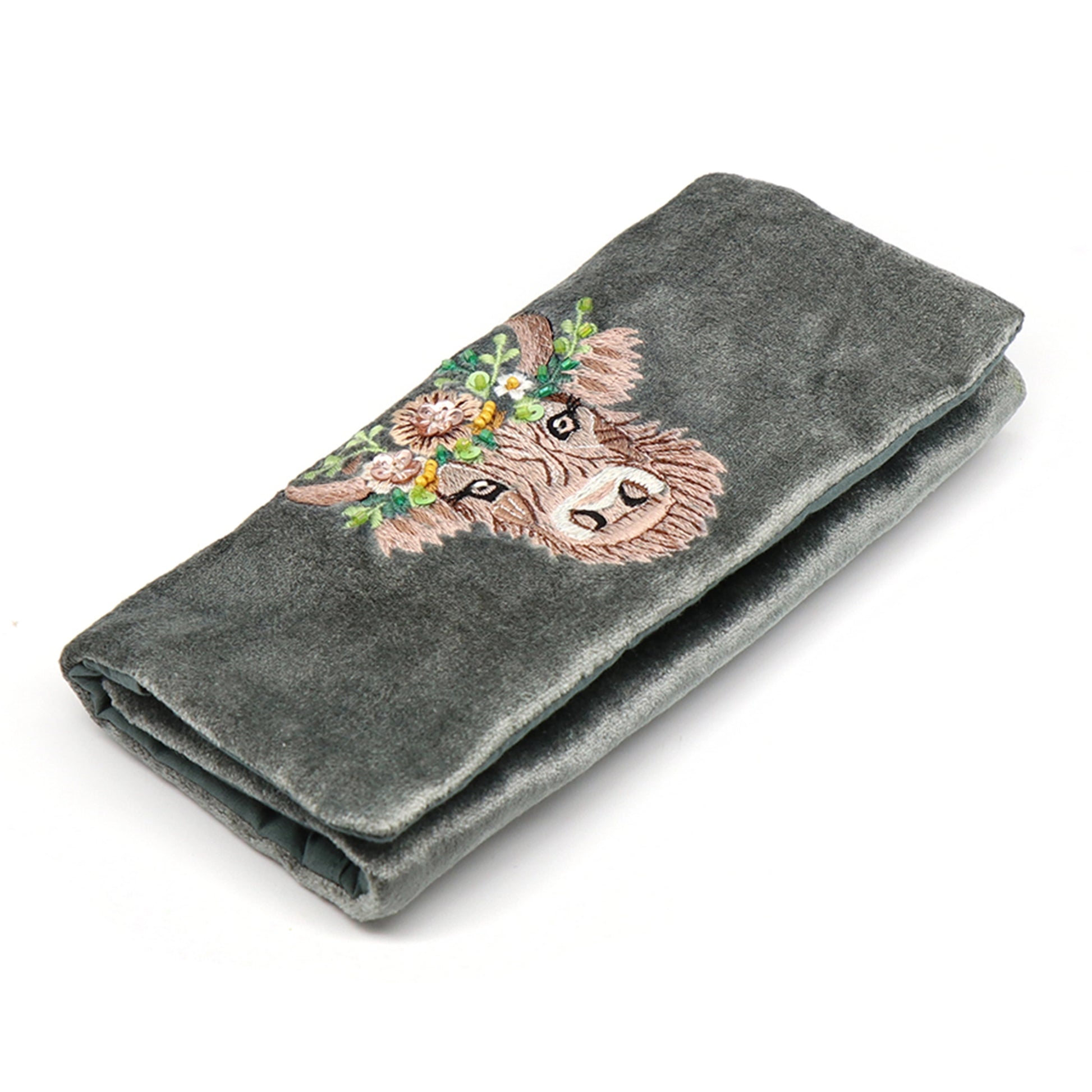 A seafoam green velvet jewellery roll with an embroidered and beaded Highland cow design
