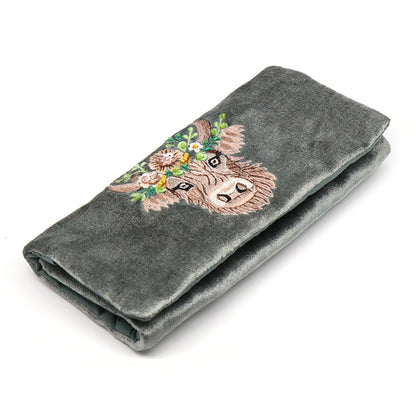 A seafoam green velvet jewellery roll with an embroidered and beaded Highland cow design