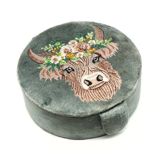 A round seafoam green velvet jewellery box with an embroidered and beaded Highland cow design