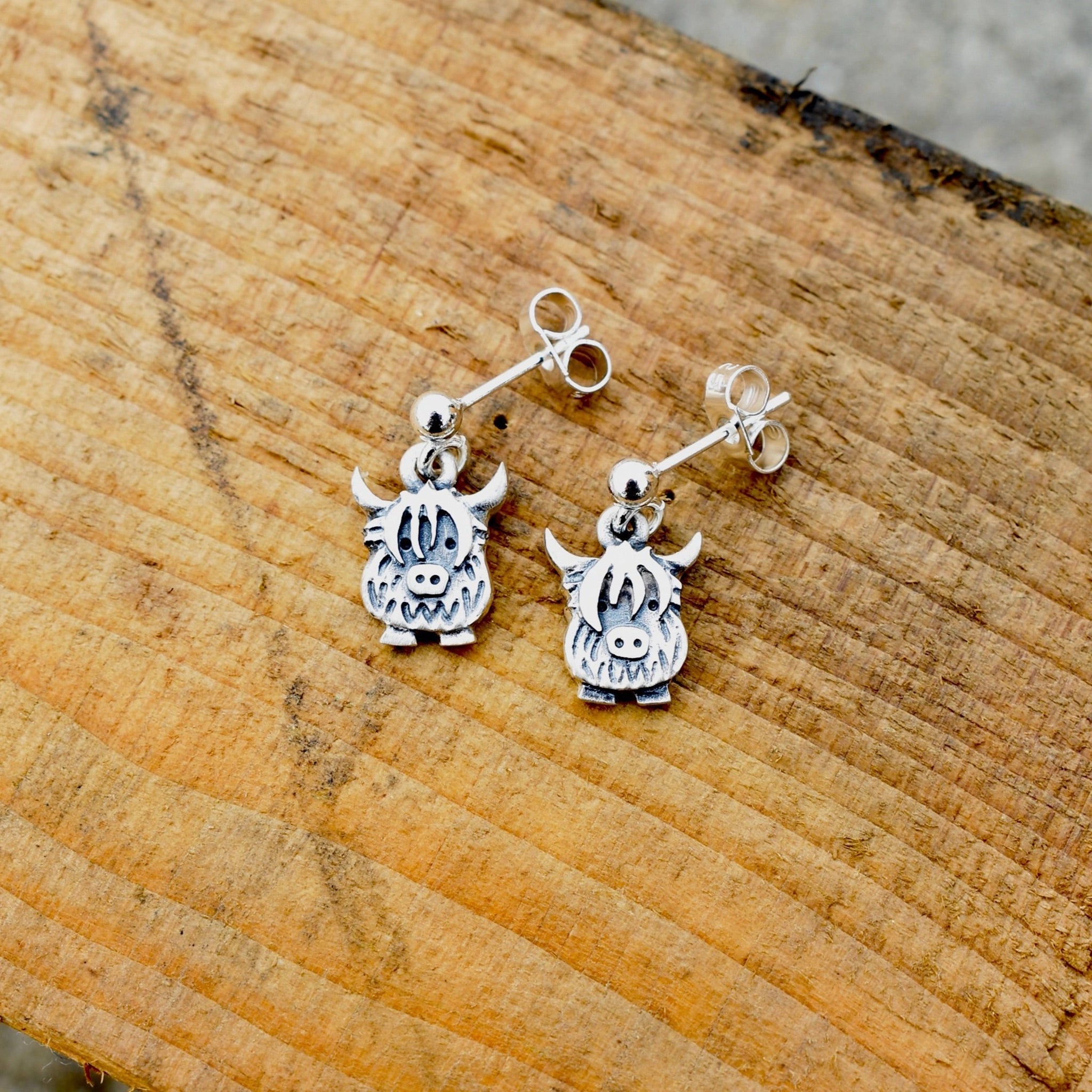 A pair of silver drop earrings shaped like Highland cows