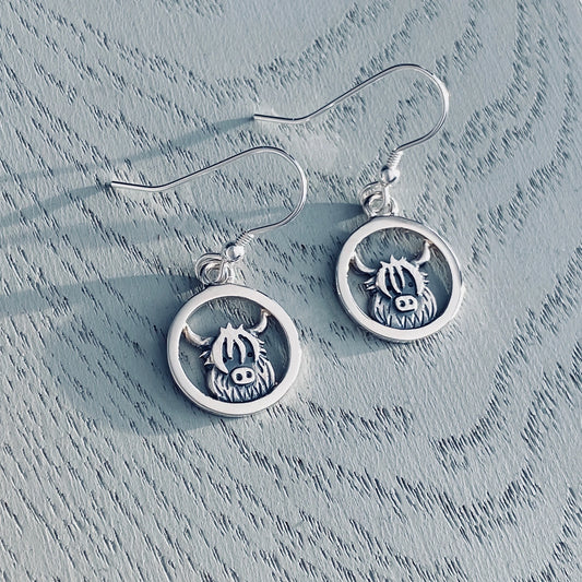 A pair of silver drop earrings featuring hooks and Highland cows inside round framesu