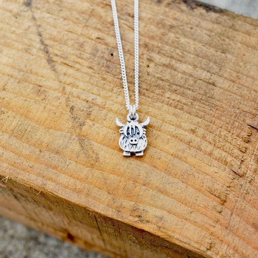 A silver pendant featuring a small Highland cow shaped charm