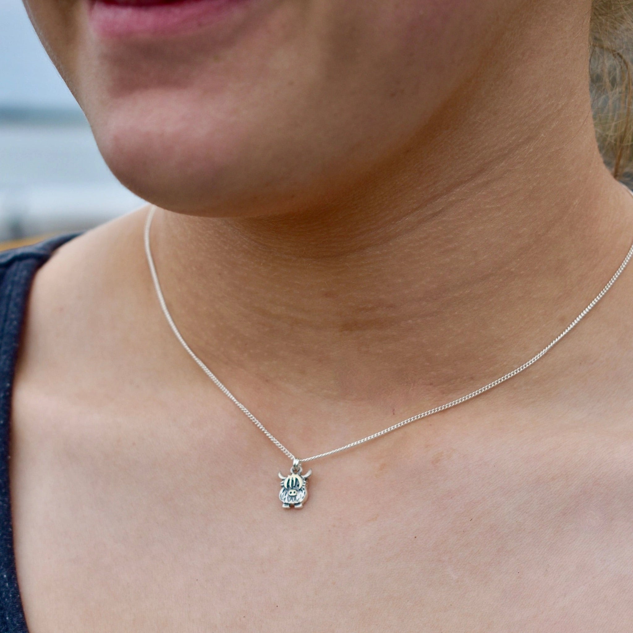 Model wearing a silver pendant featuring a small Highland cow shaped charm