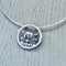 A silver necklet featuring a round pendant with a Highland cow and their calf behind a stone wall in the centre