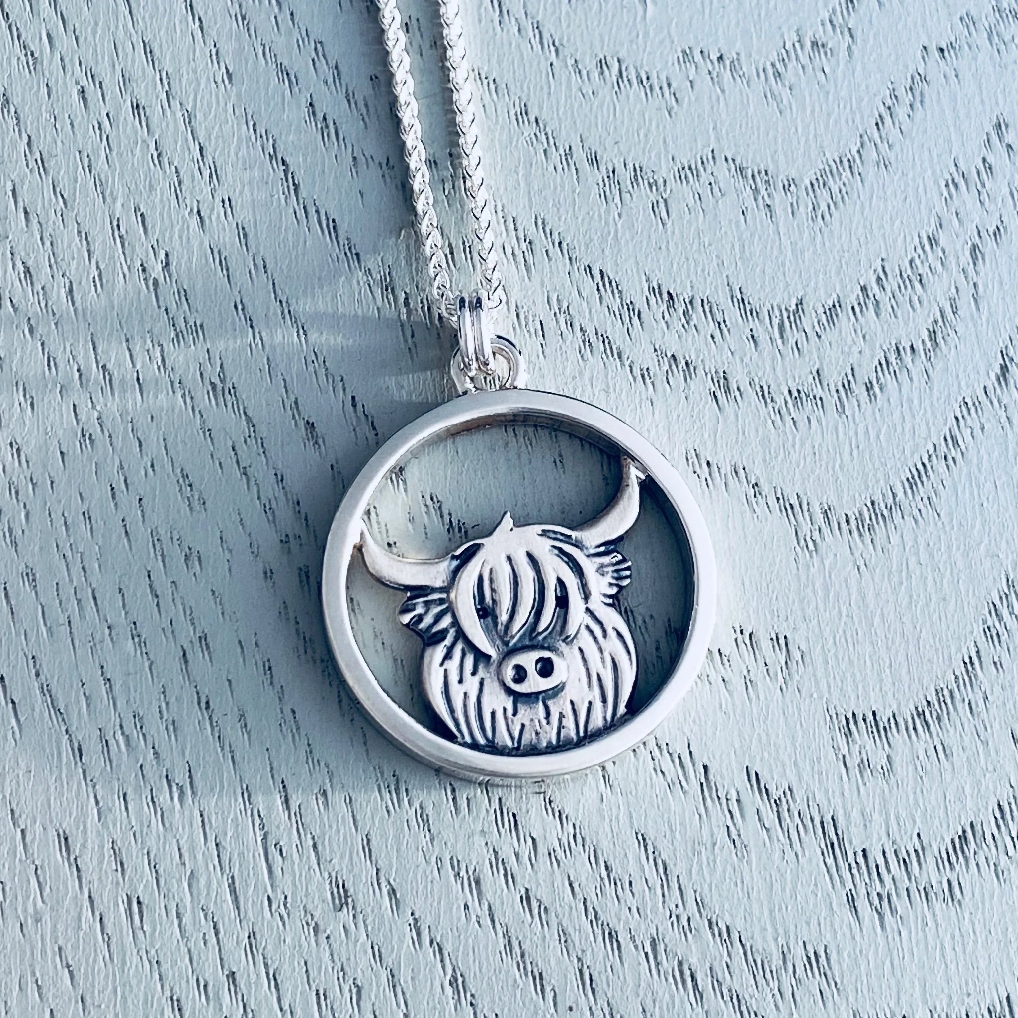 A silver pendant featuring a highland cow in a round frame on a silver chain