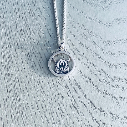 A silver pendant featuring a round frame with a Highland cow in the centre