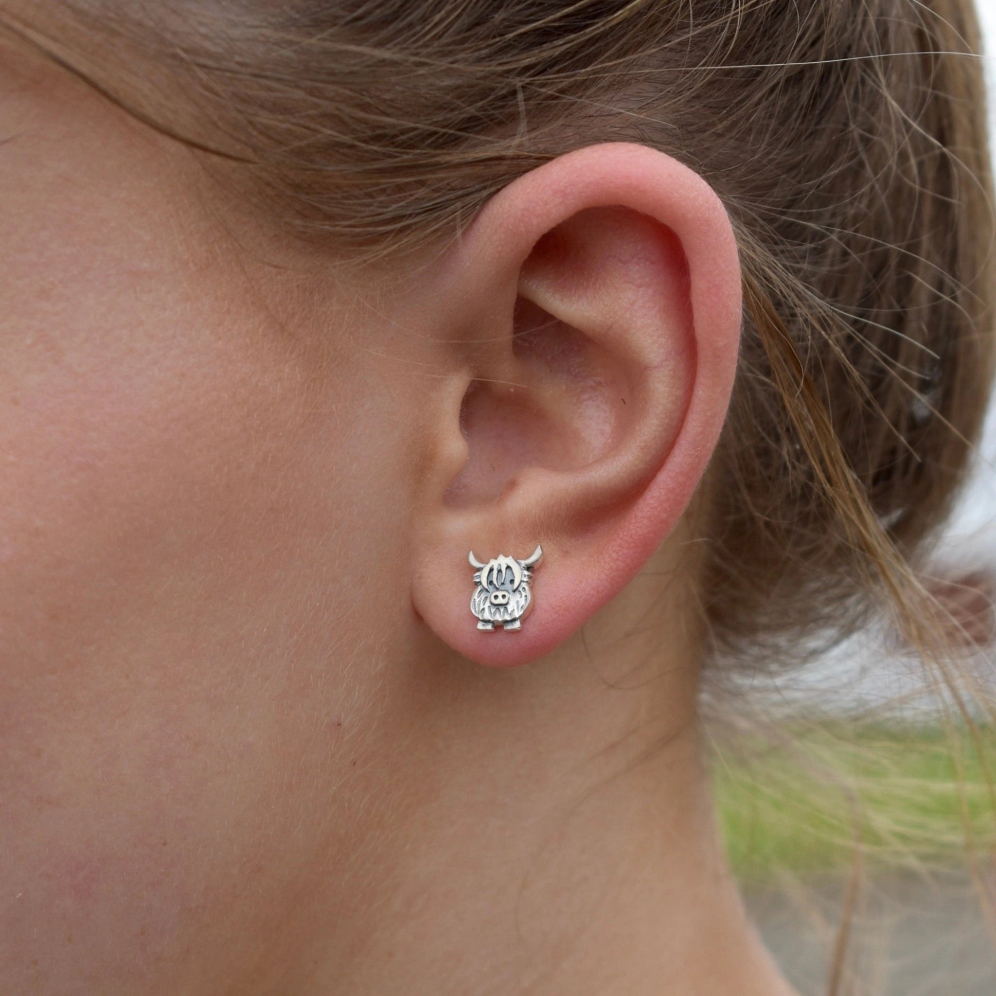 Model wearing a pair of silver stud earrings shaped like Highland cows