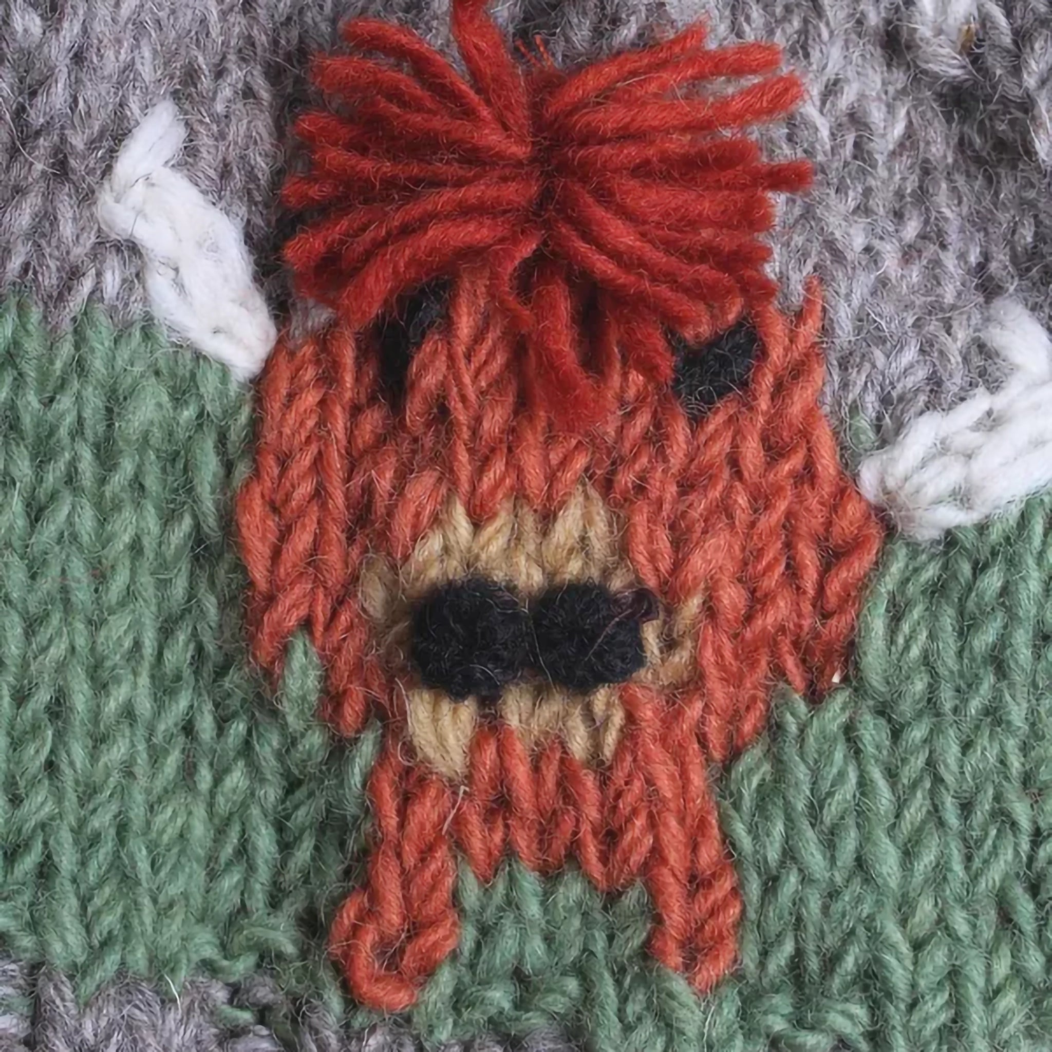 A knitted tea cosy featuring Highland cows and a pompom detail