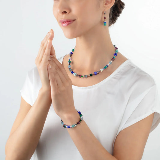 Model wearing a set of steel jewellery featuring a variety of cube shaped stones in blue and purple
