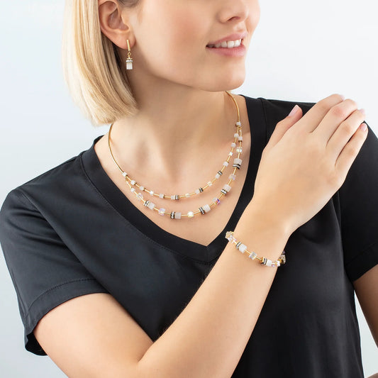 Model wearing a gold steel bracelet with white cube beads and stones