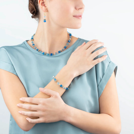 Model wearing a gold steel necklace featuring cube stones and glass beads in blue