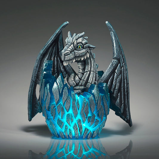 A modern sculpture of a white baby dragon hatching from an egg that lights up in blue