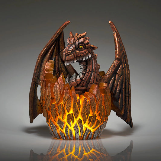 A modern sculpture of a baby dragon hatching from an egg that lights up in copper