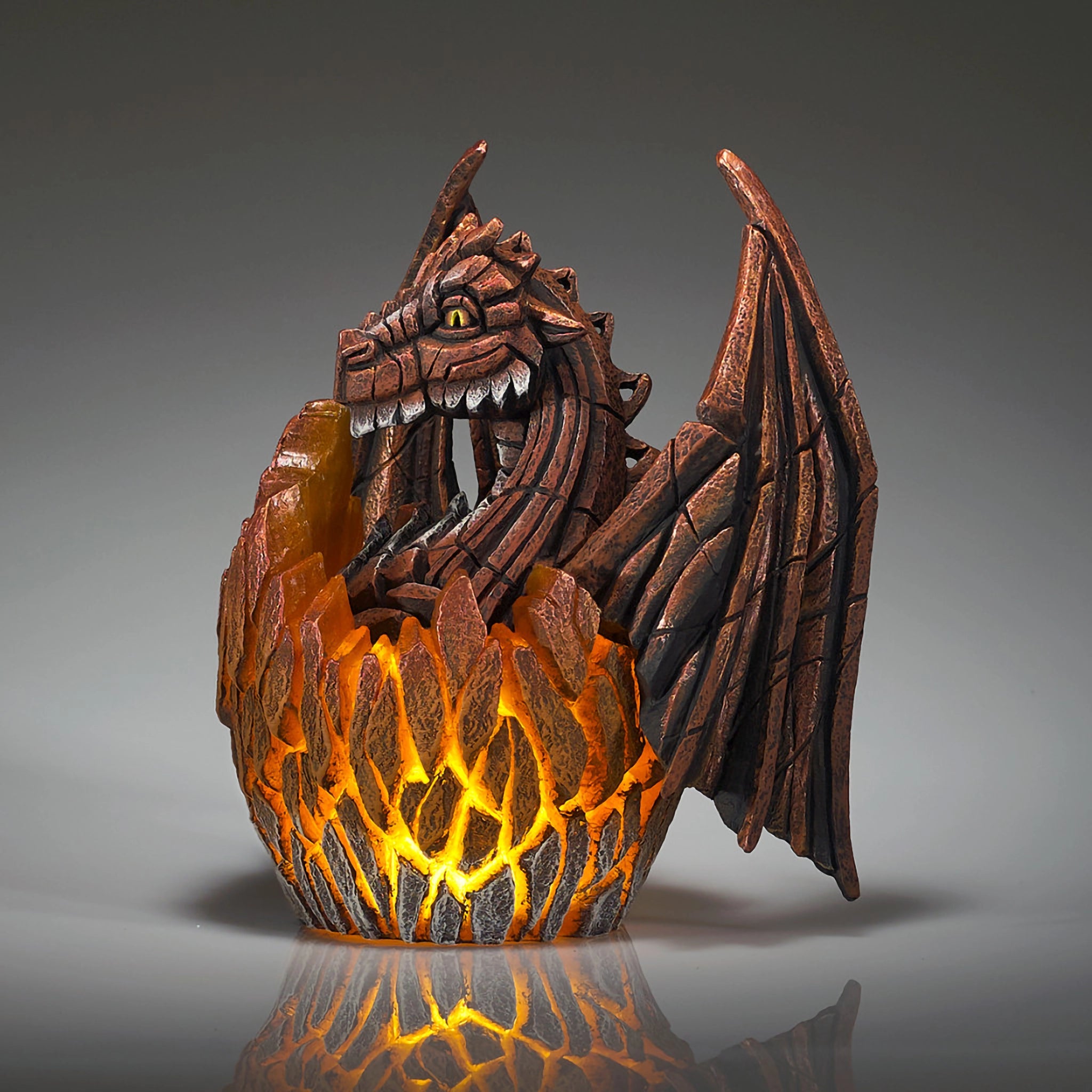 Side view of a modern sculpture of a baby dragon hatching from an egg that lights up in copper