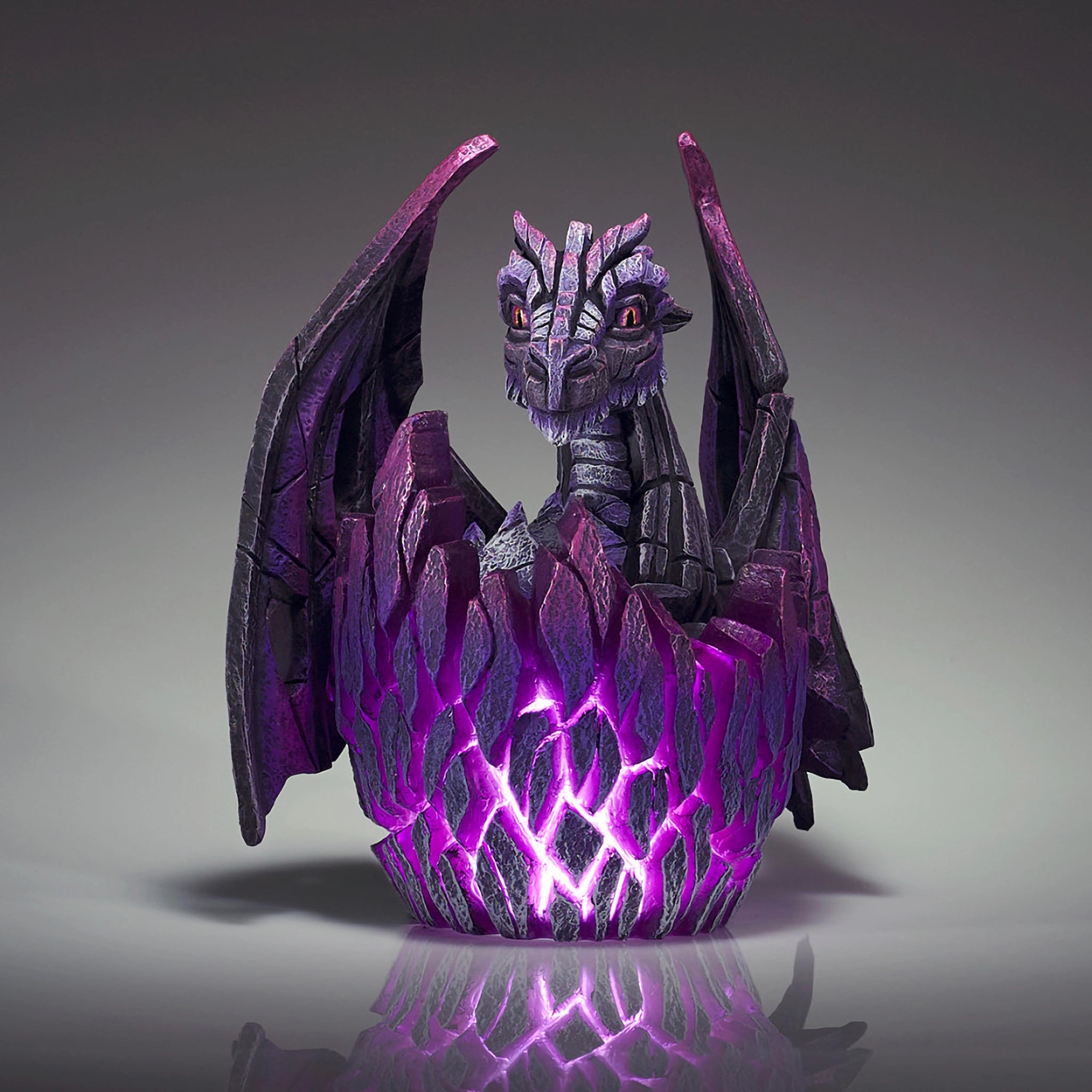 Front view of a modern sculpture of a black baby dragon hatching from an egg that lights up in purple