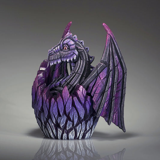 Side view of a modern sculpture of a black baby dragon hatching from an egg 