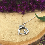 Posed silver pendant with irregular round shape, a bunny and tree design and a gold heart detail on silver chain