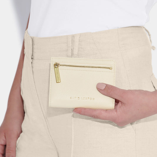 Model holding little ecru purse branded with 'Katie Loxton' and featuring a gold zip
