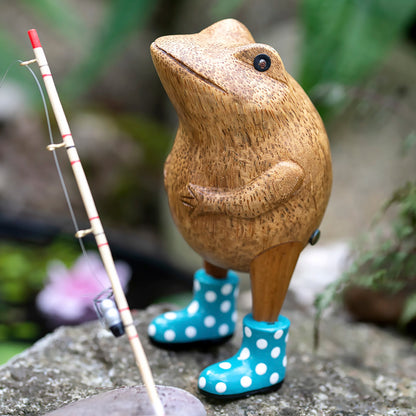 Wooden frog figurine with blue spotted wellies posed outside with a fishing rod