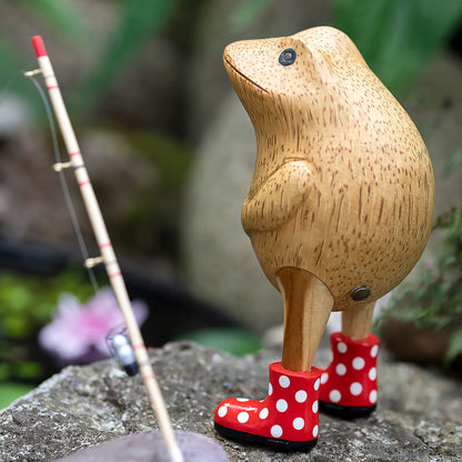Wooden frog figurine with red spotted wellies posed on a rock with a fishing rod