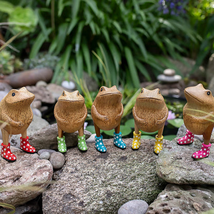 Wooden frog figurines with spotted wellies posed outside on rocks
