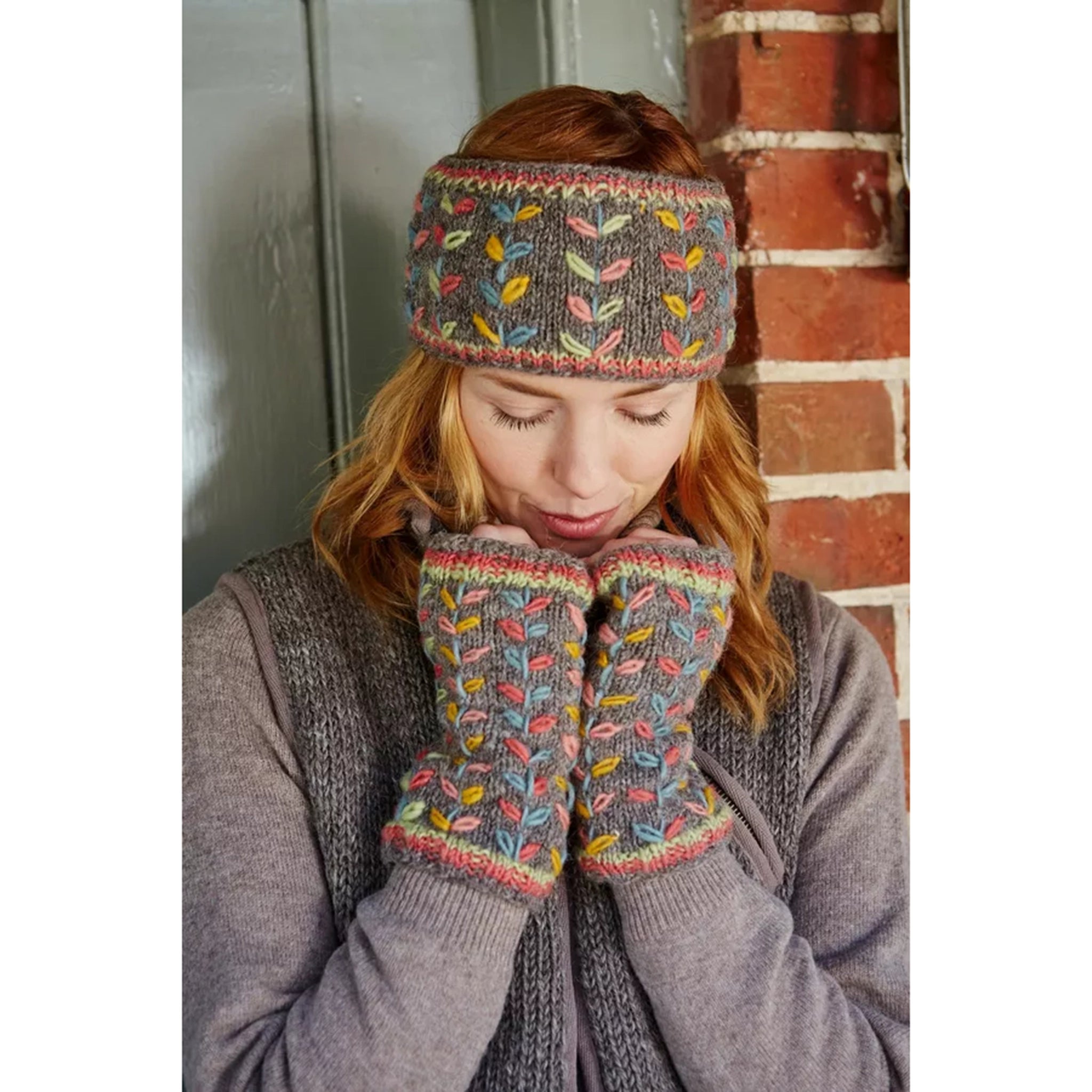 Model wearing a pair of knitted grey handwarmers with multicolour running leaf 