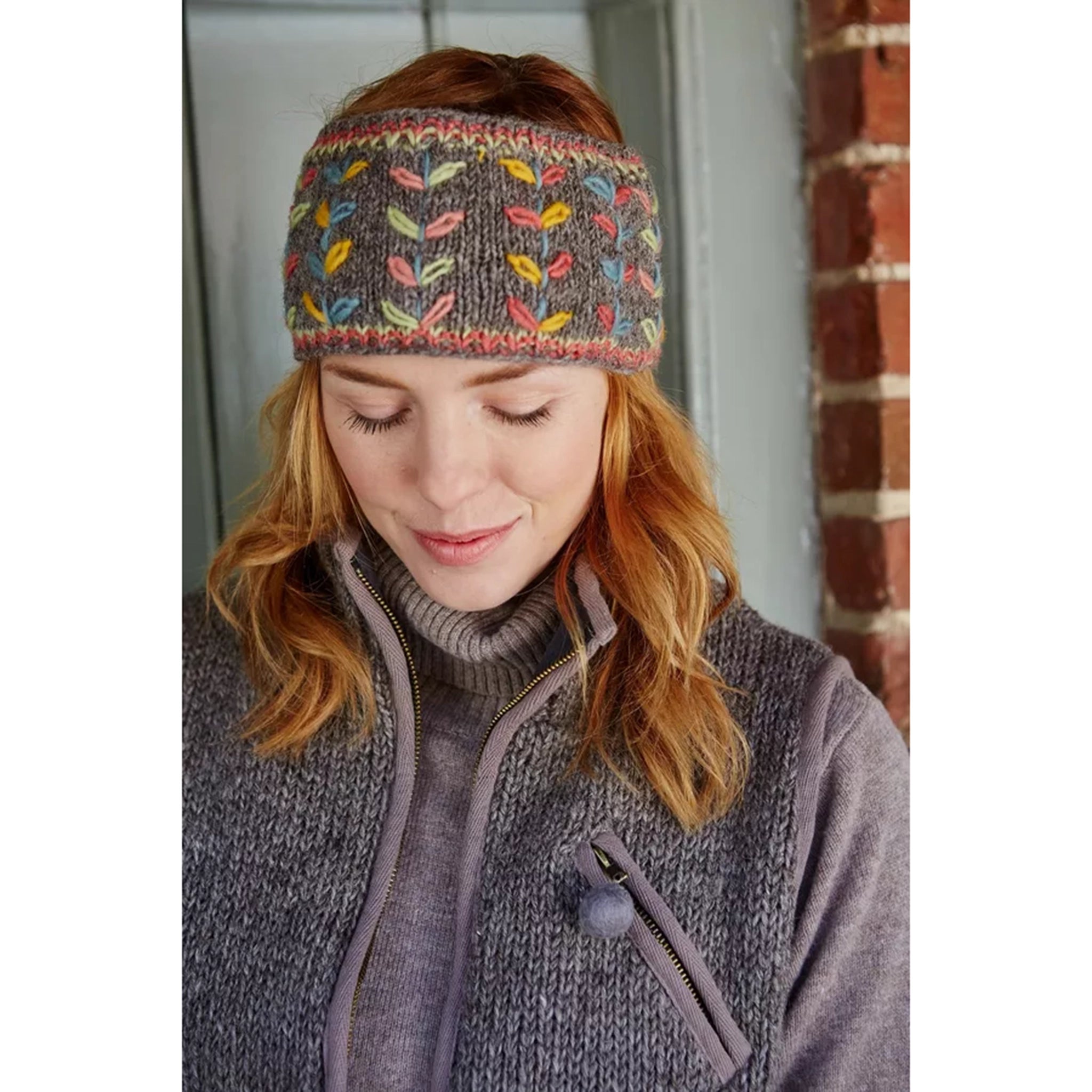 Model wearing a knitted grey headband with multicolour running leaf patterns.