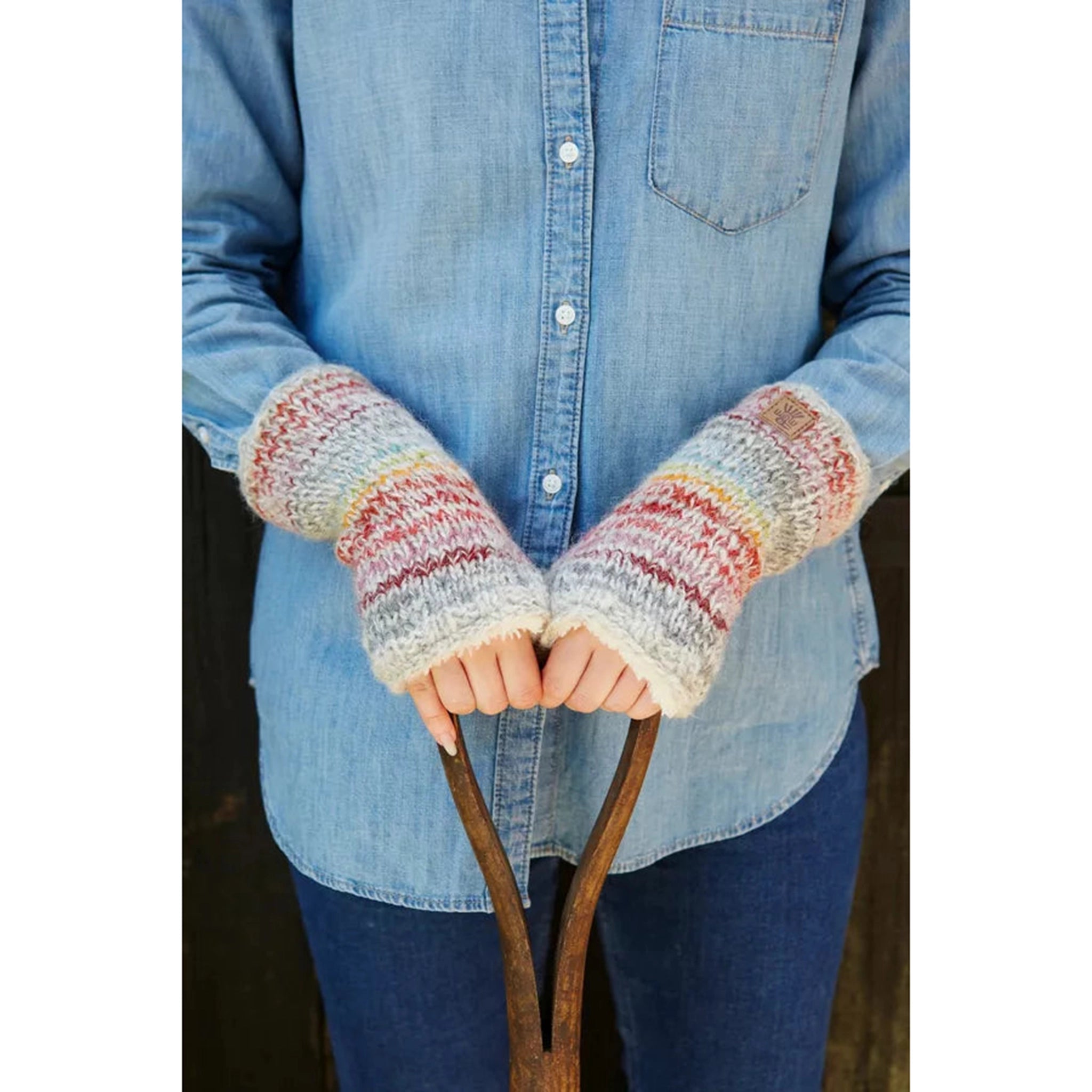 Model wearing a pair of knitted handwarmers in light grey with thin multicoloured stripes.