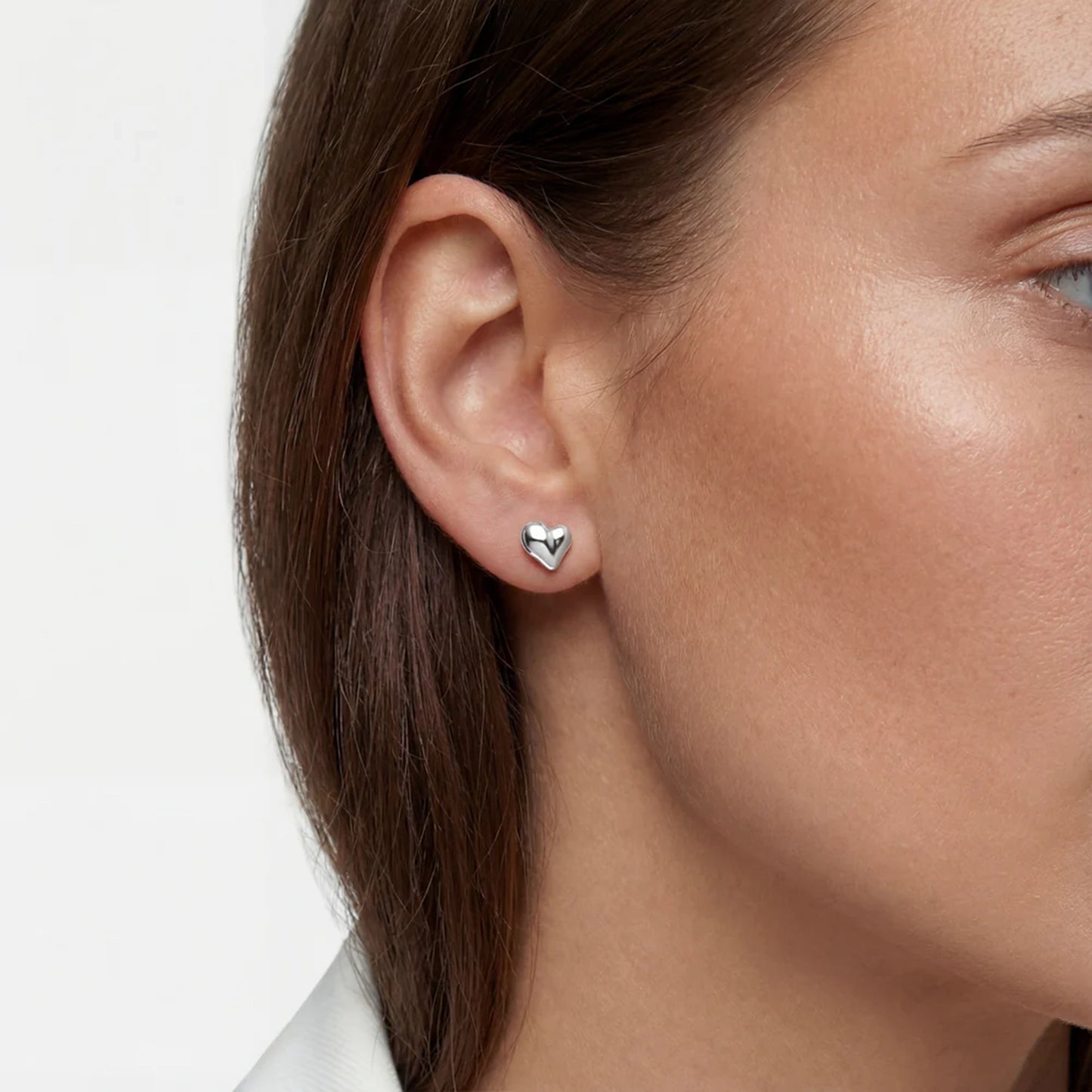 Model wearing silver stud earrings shaped like puffy asymmetrical hearts