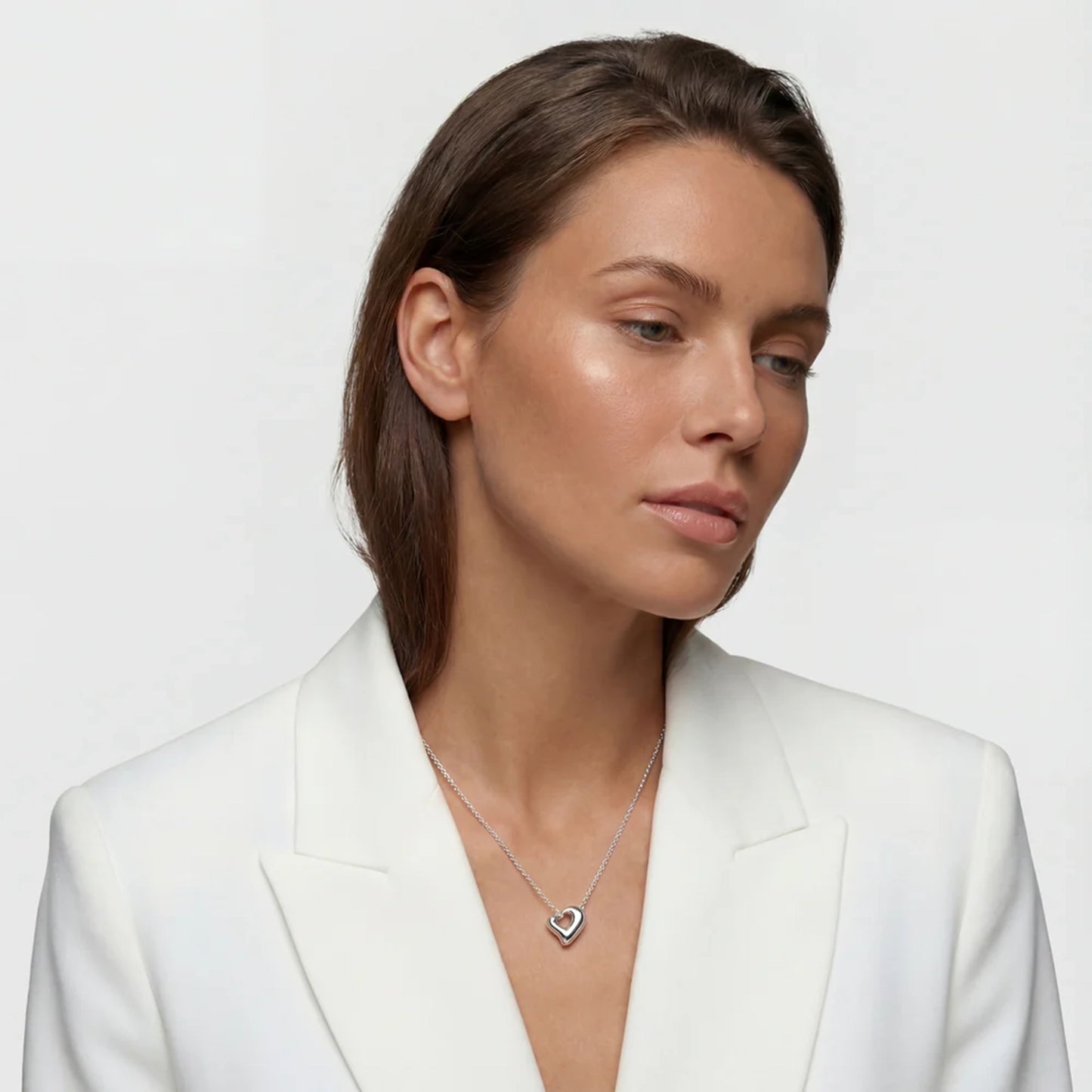 Model wearing silver necklace shaped like an open puffy asymmetrical heart on a silver chain