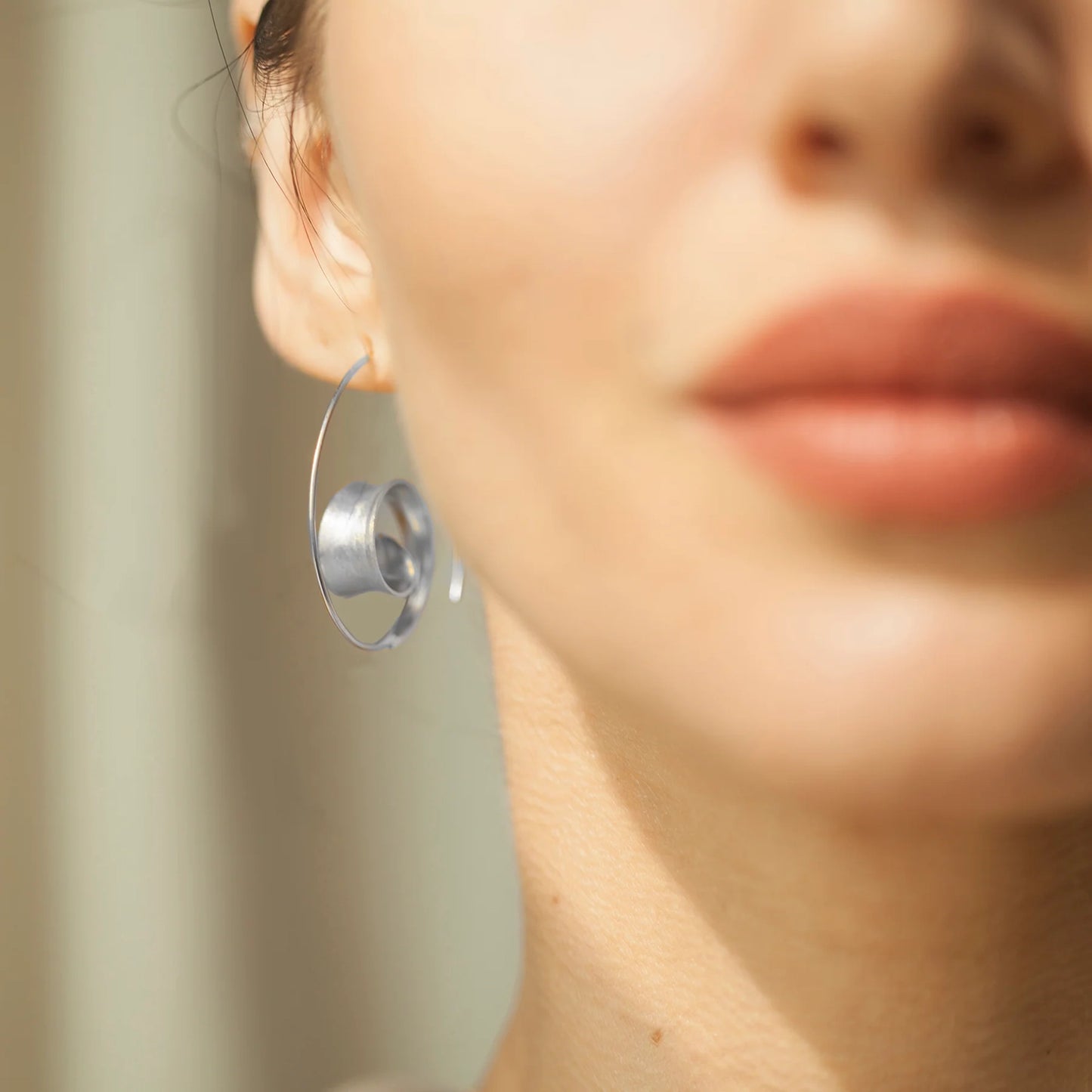 Model wearing satin finish silver spiral earrings with long hooks and curled leaf design