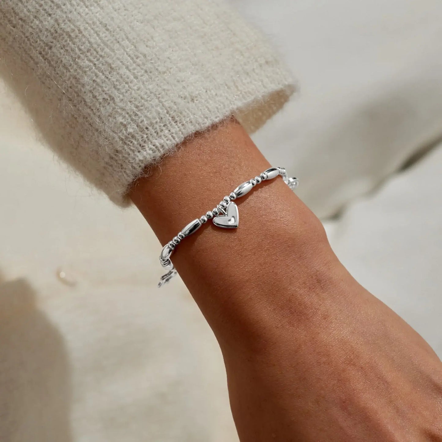 A beaded stretch silver bracelet with three different heart charms on model