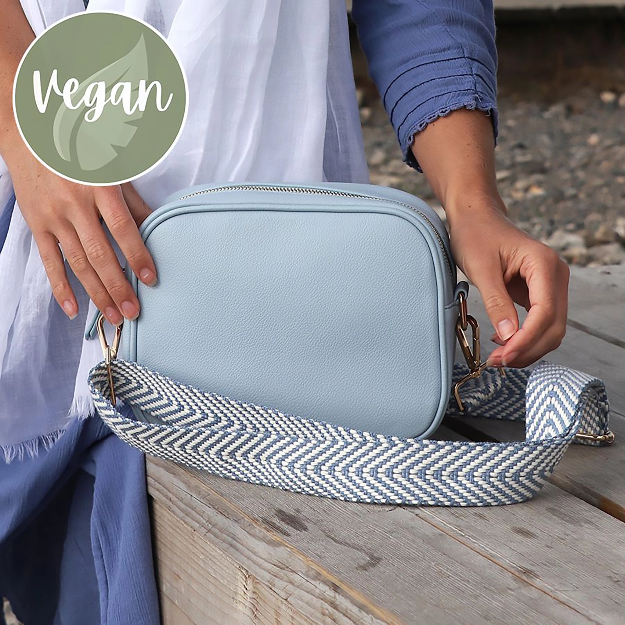 Model with light blue vegan leather cross body camera bag with white and grey simple chevron print woven strap