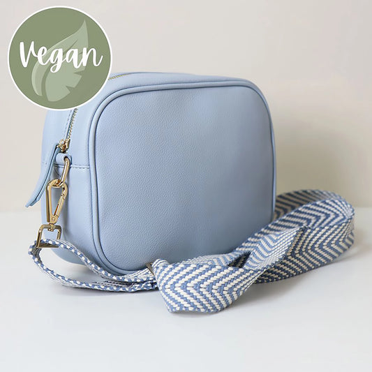 Side view of light blue vegan leather cross body camera bag with white and grey simple chevron print woven strap