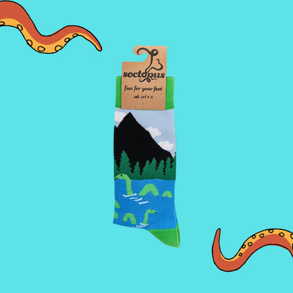 Blue and green socks with loch ness monster design with cardboard packaging hanger