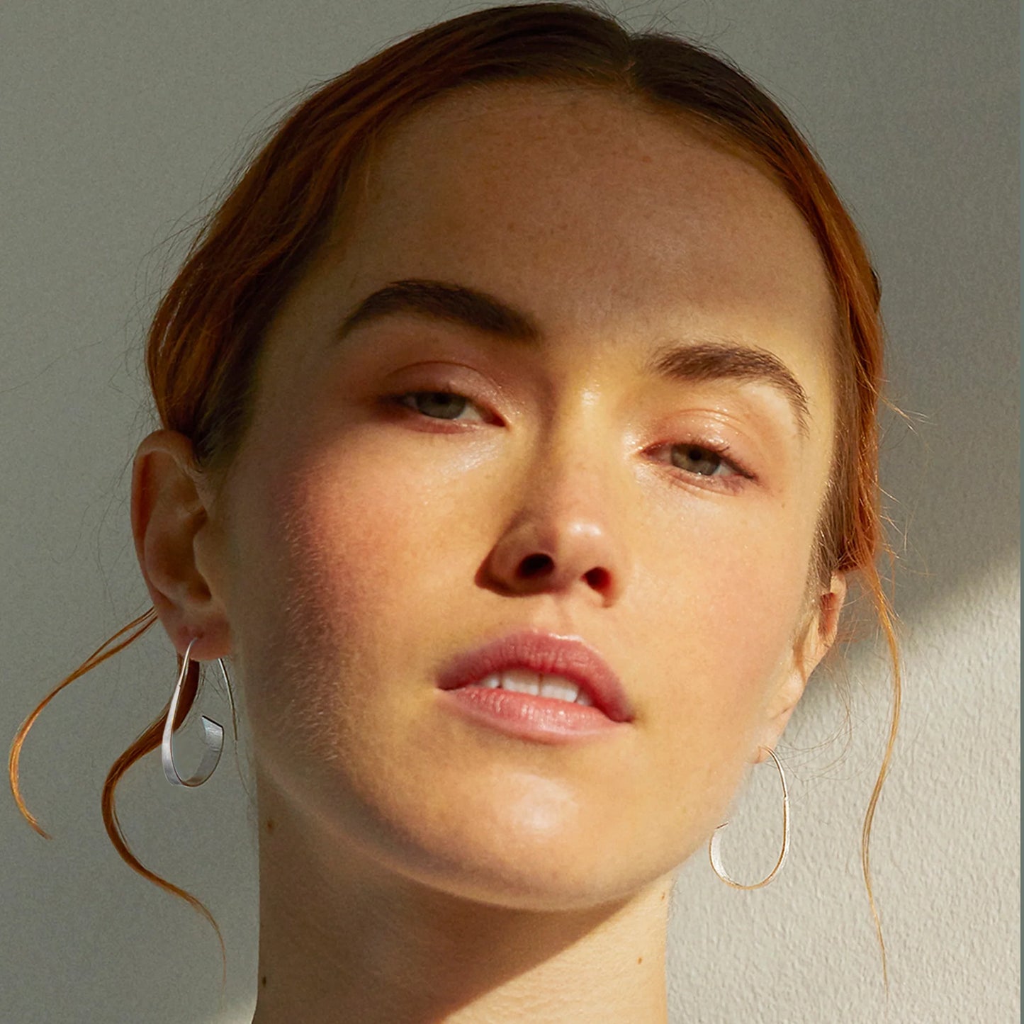 Model wearing satin finish silver spiral earrings with long hooks and curled ribbon design