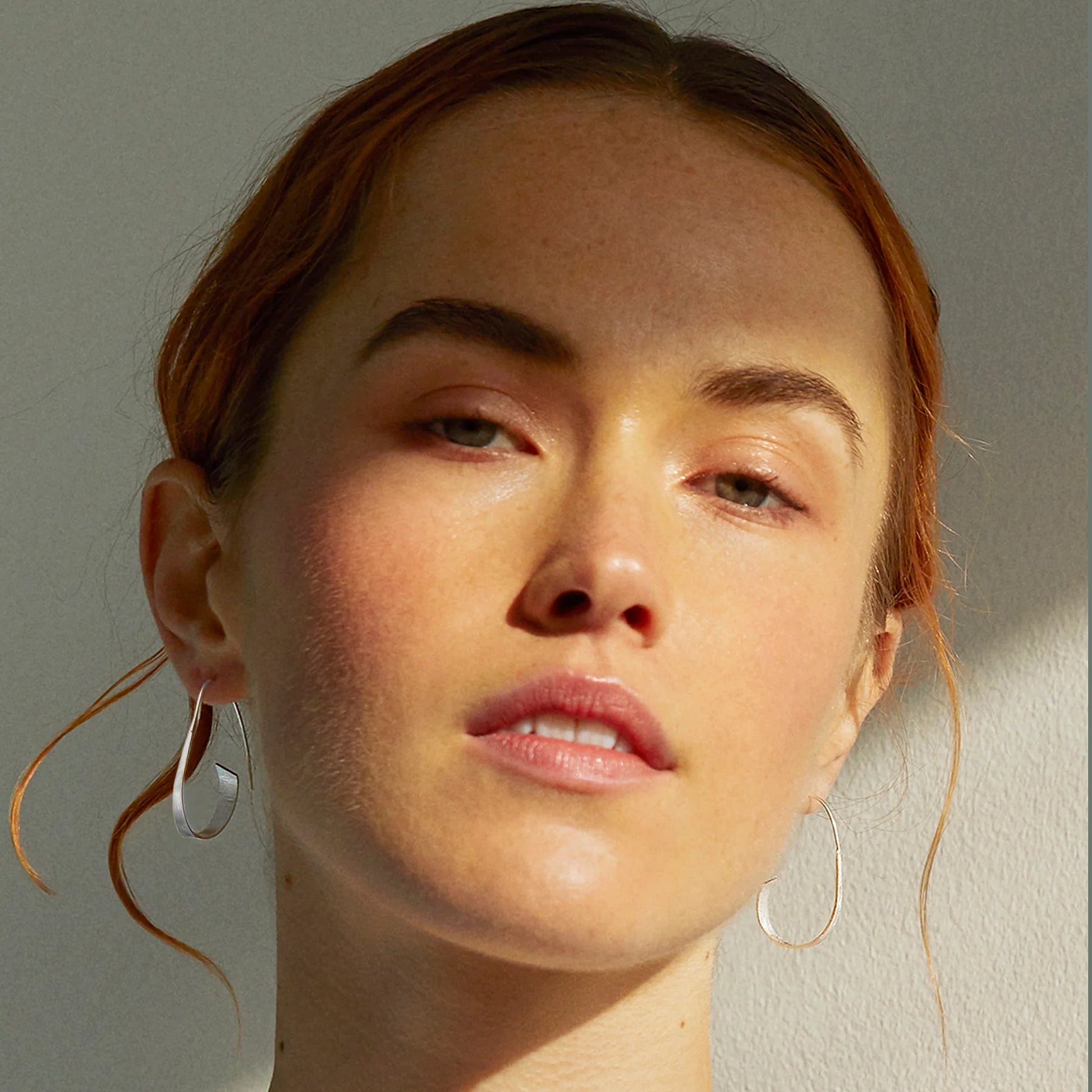 Model wearing satin finish silver spiral earrings with long hooks and curled ribbon design