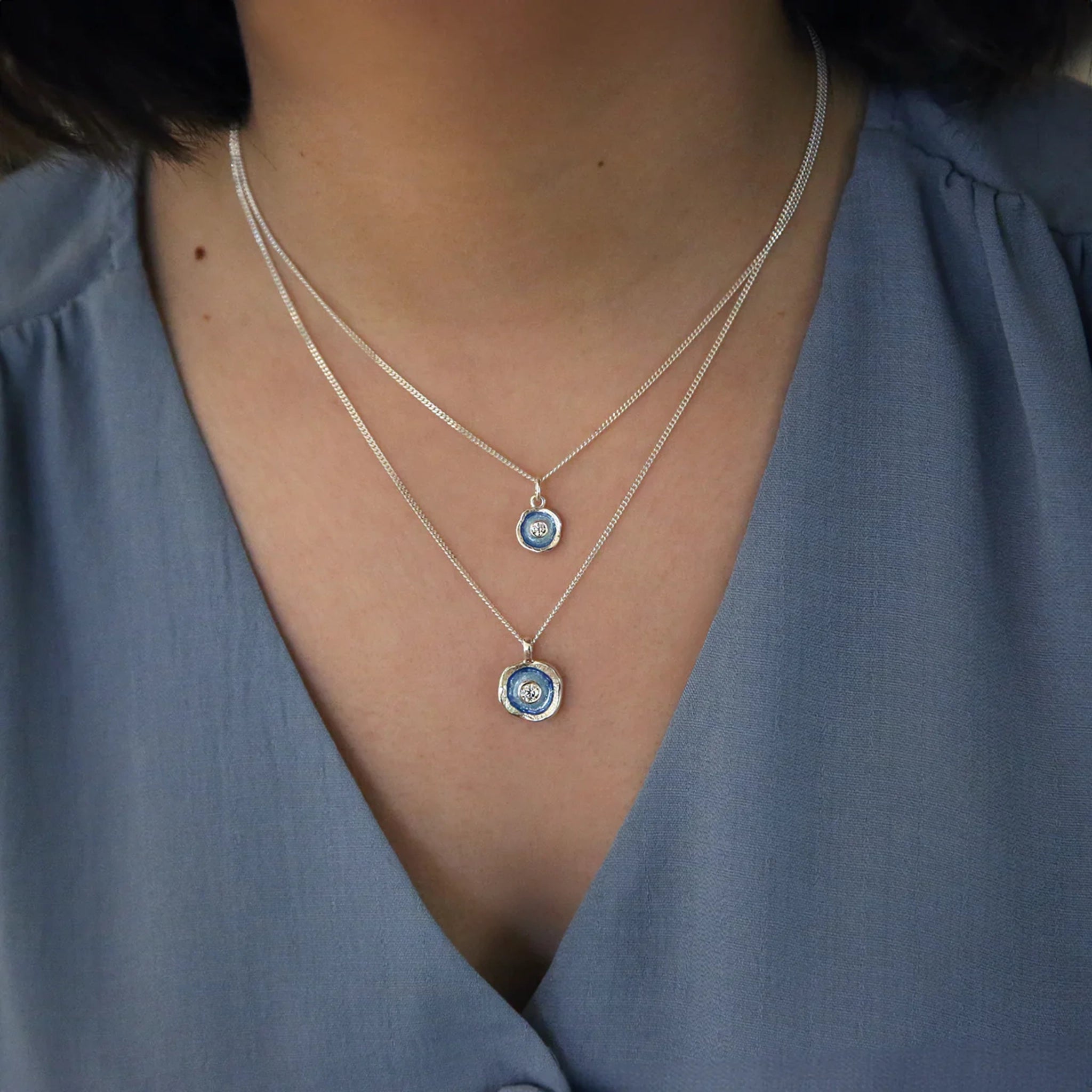 Model wearing a silver pendant featuring a round organic shape with a CZ in the centre and light blue enamel