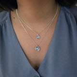 Model wearing a silver pendant featuring a round organic shape with a CZ in the centre and light blue enamel