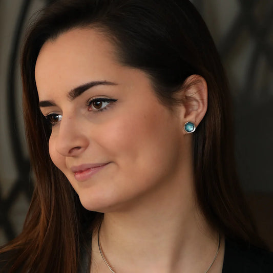 Model wearing silver round stud earrings with organic shape and subtle texture and blue green enamel centres