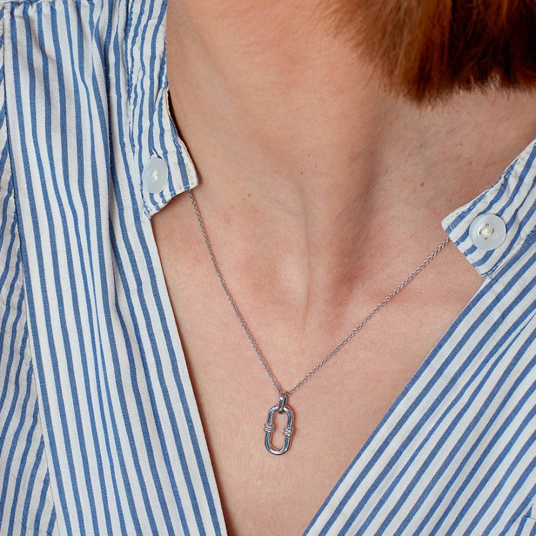 Model wearing a silver pendant shaped like a single chain link with twisted rope details