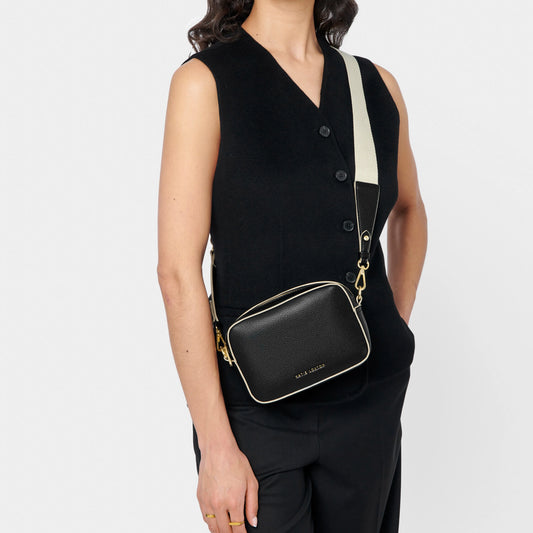 Model wearing a black cross-body bag with contrast wax piping in light sand