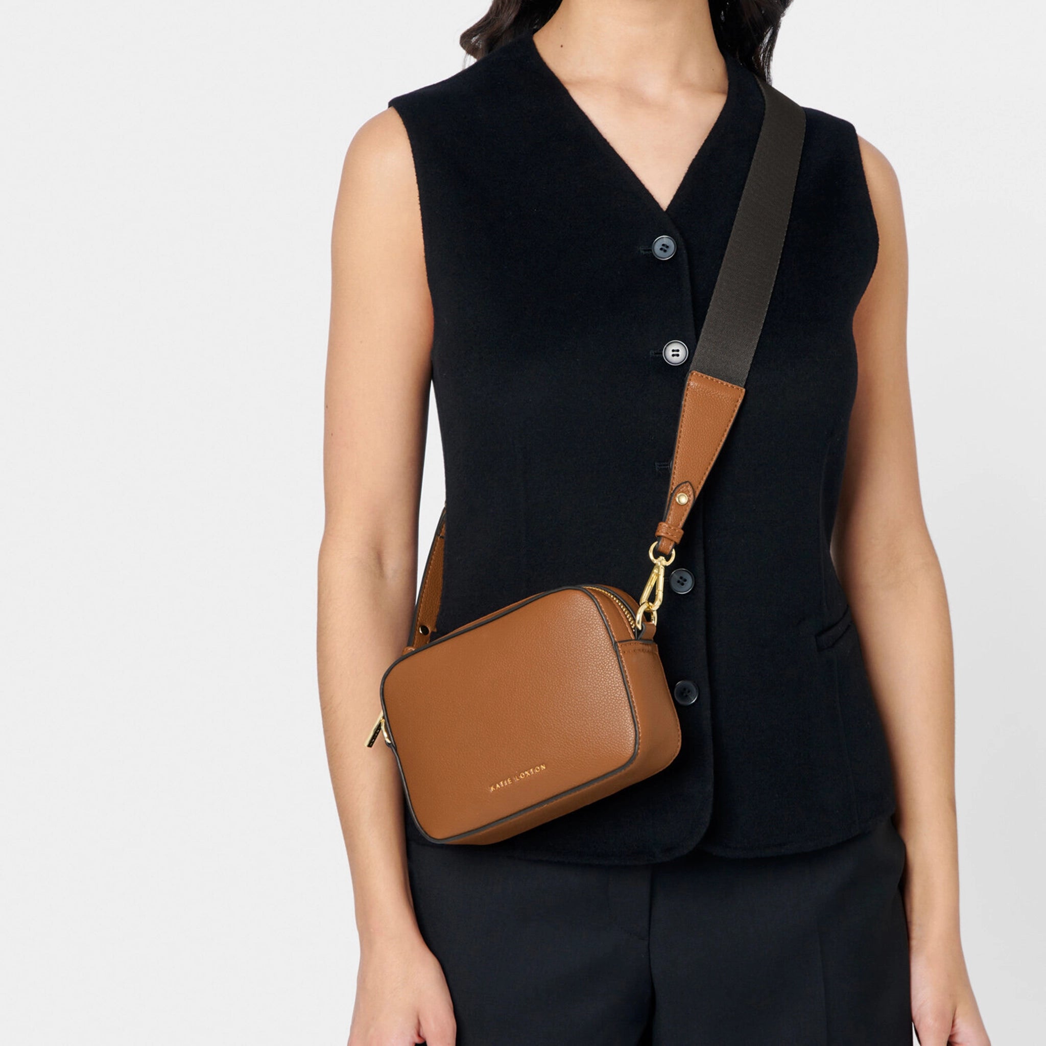 Model wearing a brown cross-body bag with contrast wax piping in black 