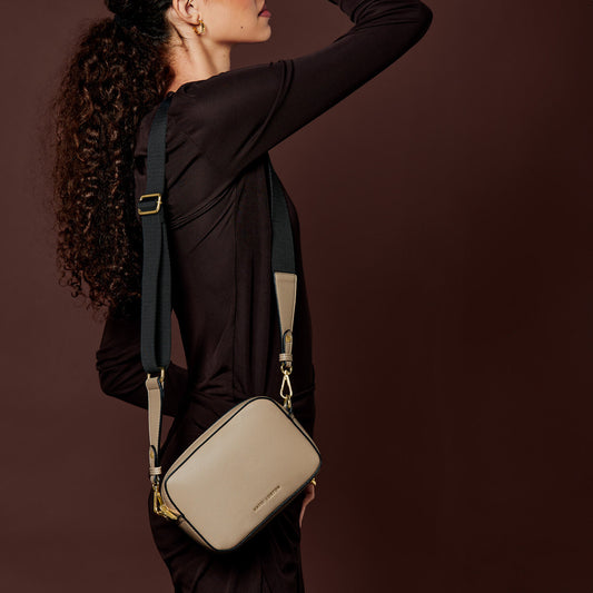 Model wearing a taupe cross-body bag with contrast wax piping in black